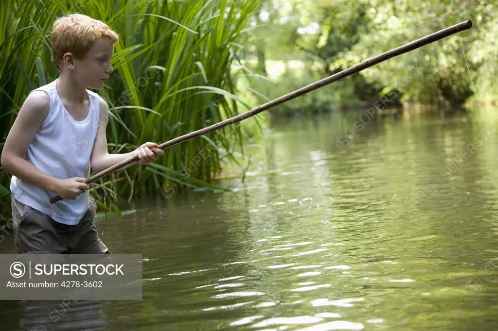 Young boy fishing in a river with his legs in the water