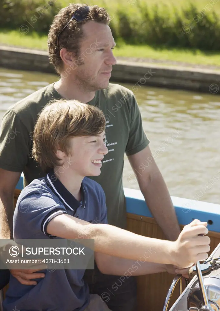 Man and smiling teenaged boy steering a boat