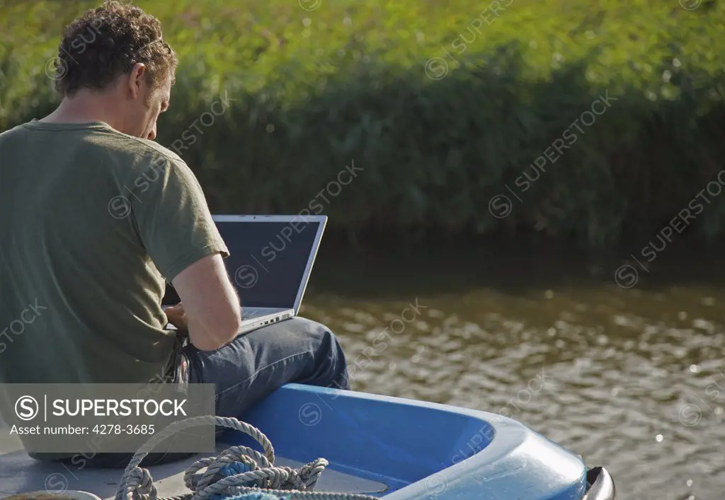 Back view of a man sitting on a boat using a laptop computer