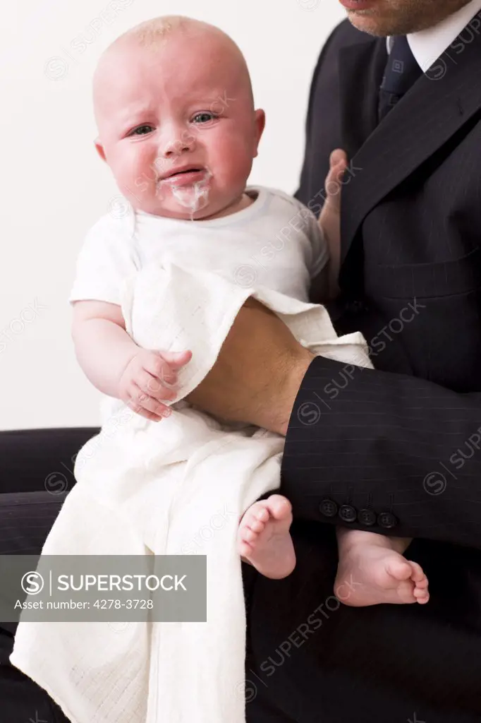 Baby boy sitting on a businessman lap crying and throwing up