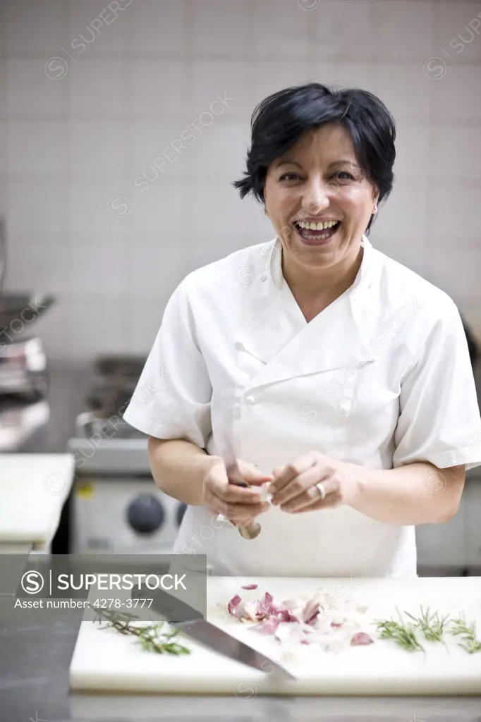 Woman chef peeling garlic with a knife and smiling