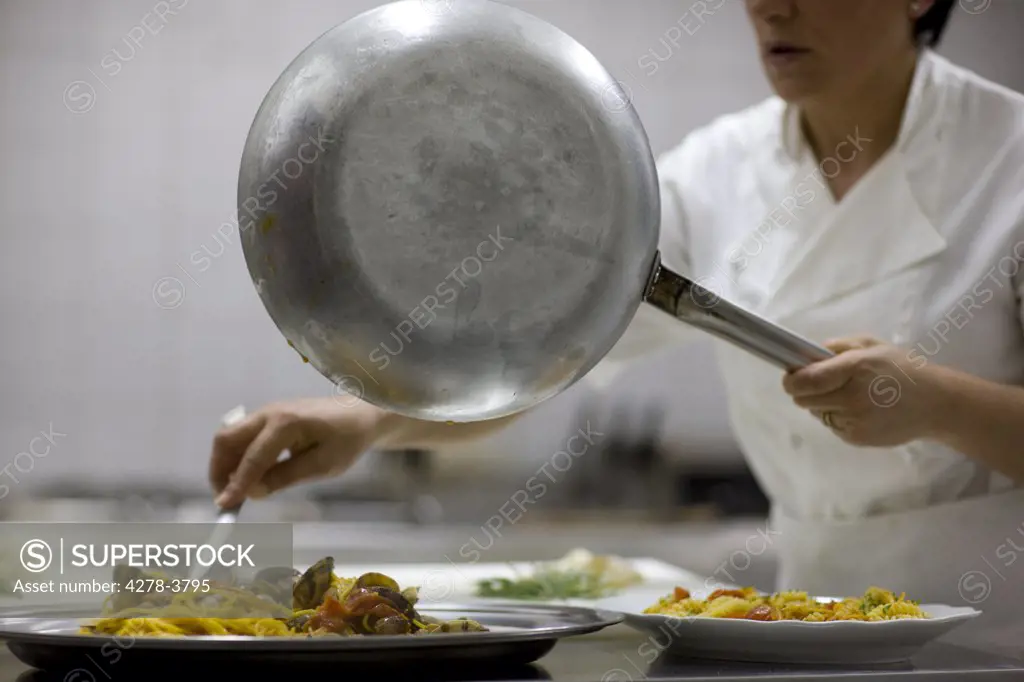 Woman chef holding a frying pan and preparing seafood pasta for service