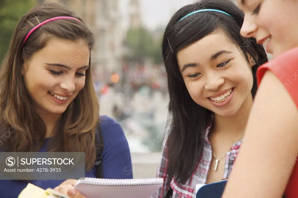Three smiling teenaged girls reading, writing and holding note pads