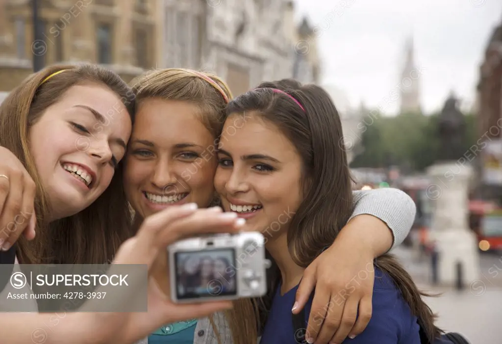 Three smiling teenaged girls taking a self-portrait with digital camera in London, England