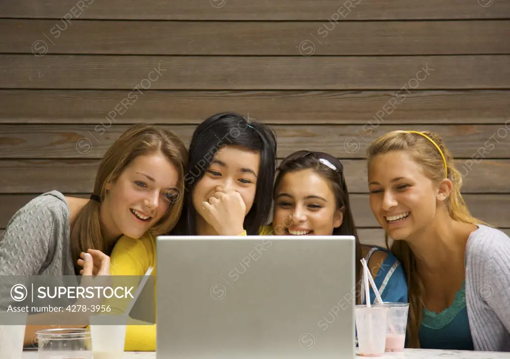 Teenage girls sitting in front of laptop computer laughing