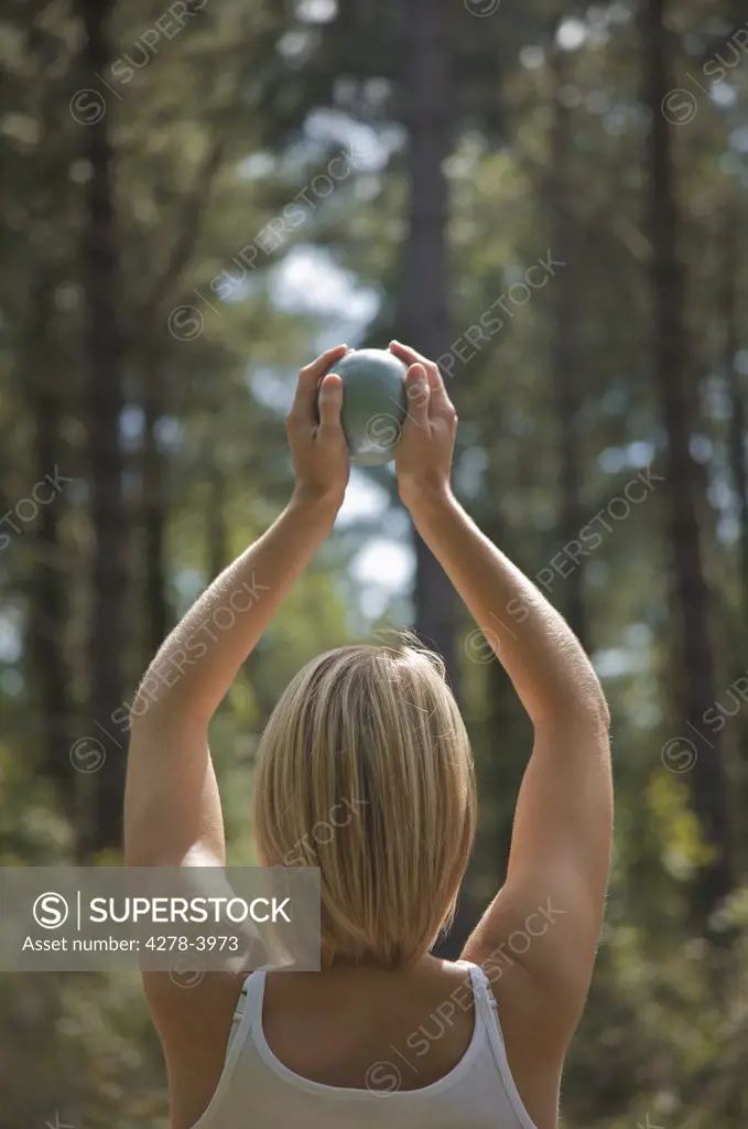 Back view of a young woman with arms stretched holding a sphere