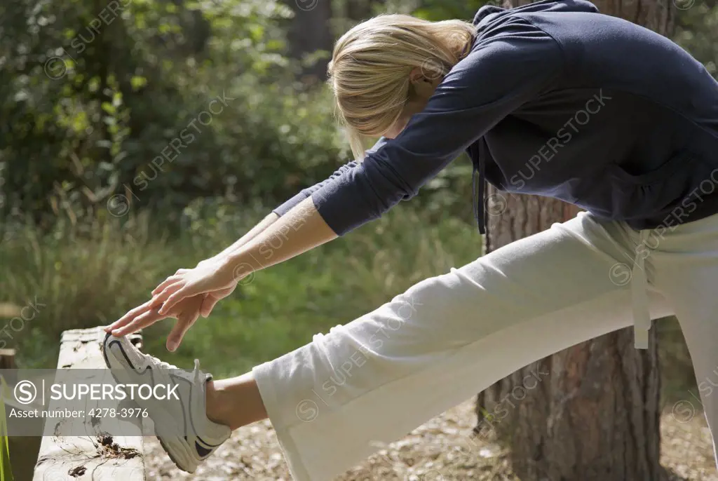 Young woman in a forest stretching her leg over a wooden beam and touching her foot