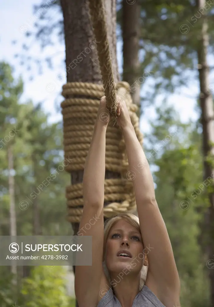 Young woman at obstacle course hanging from a rope