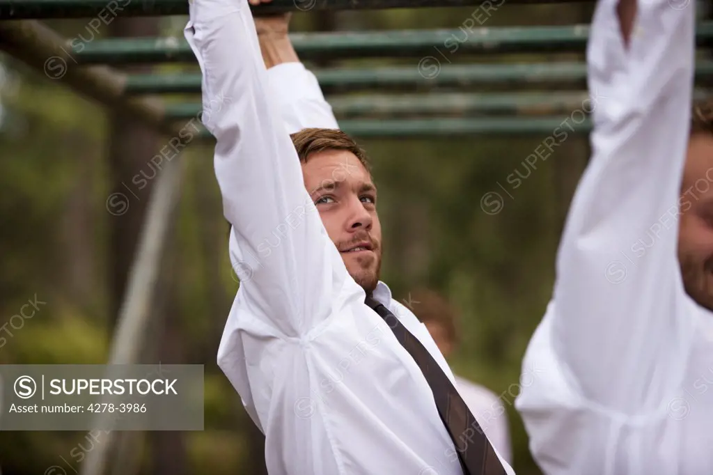 Businessman at an obstacle course dangling from parallel bars