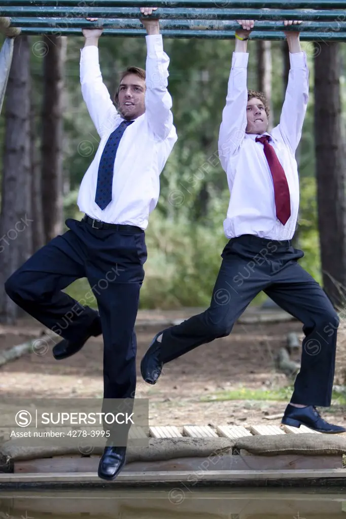Two businessmen at an obstacle course dangling from parallel bars