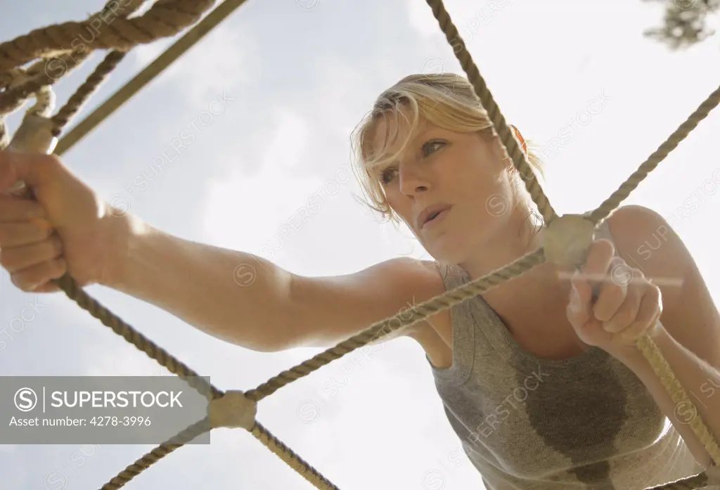 Young woman at obstacle course climbing a cargo net