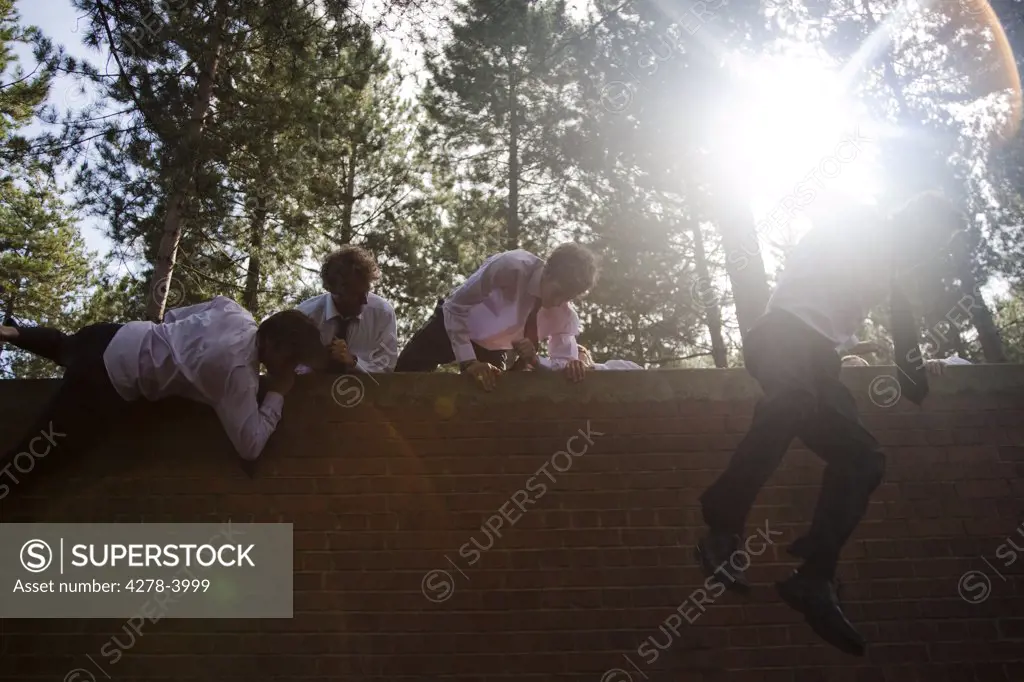 Businessmen at an obstacle course climbing a brick wall