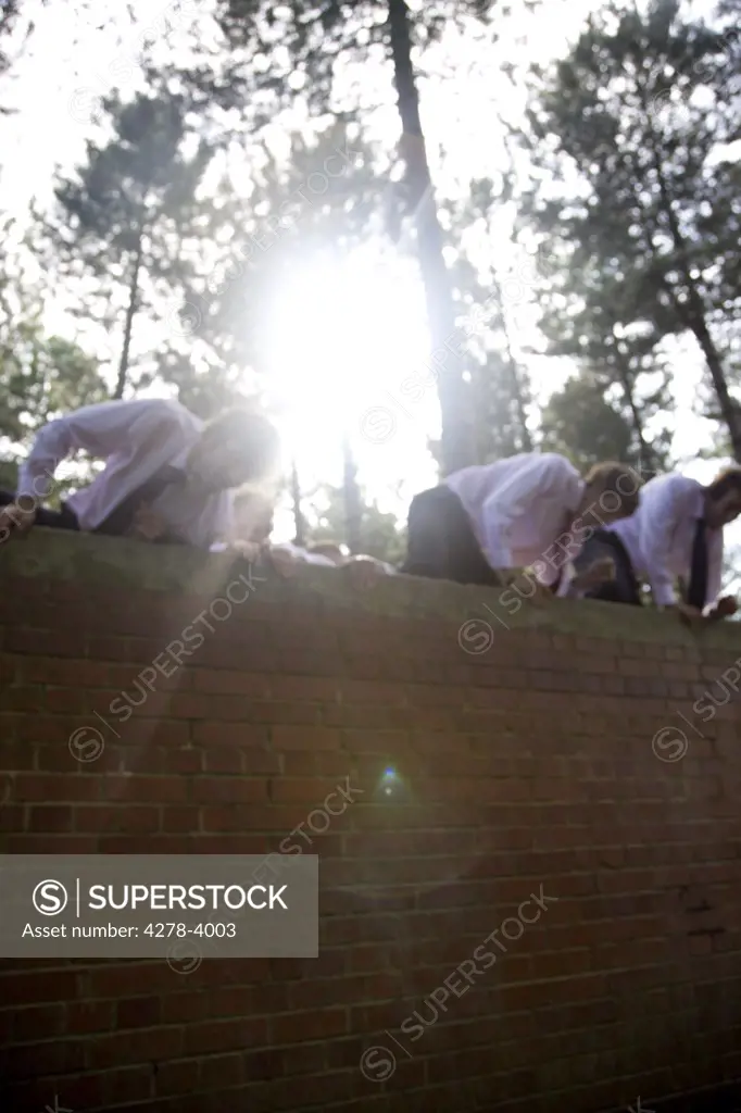 Businessmen at an obstacle course climbing a brick wall