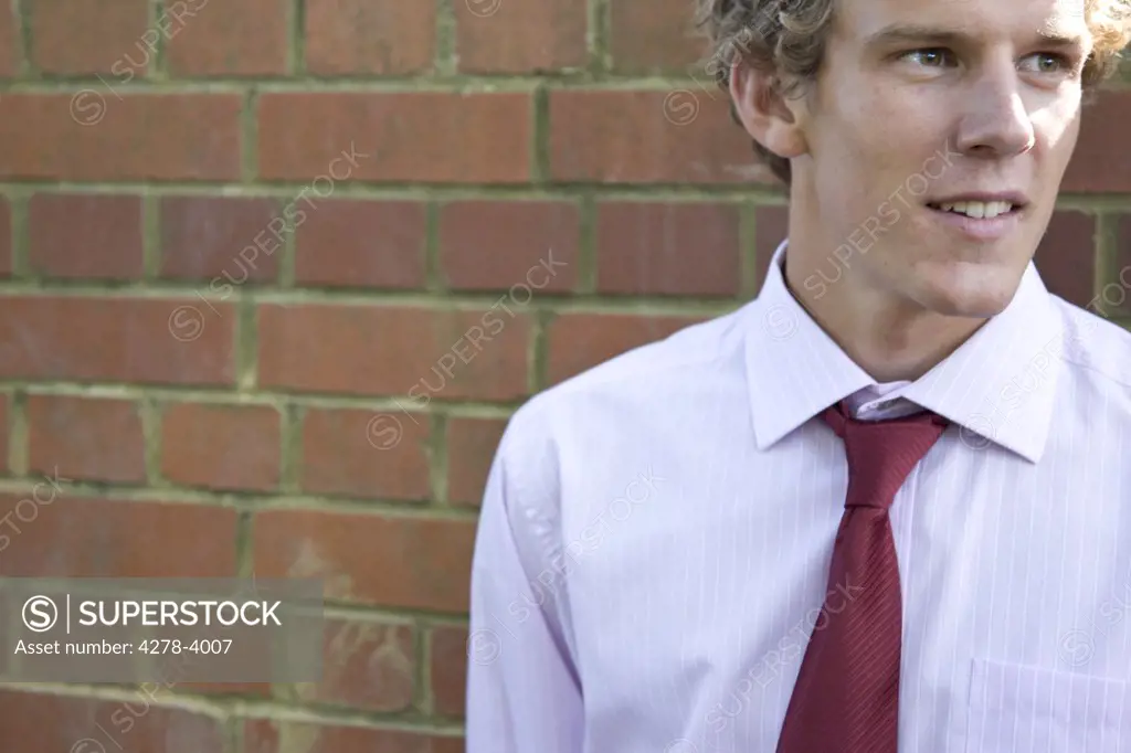 Young businessman standing against brick wall