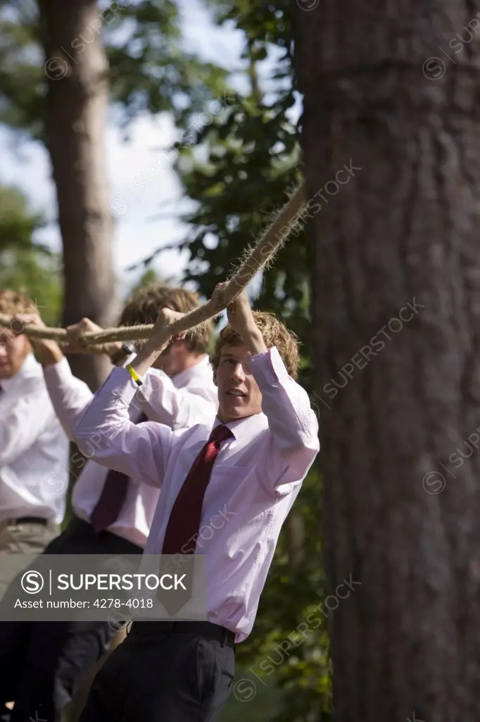 Businessmen at an obstacle course hanging from a rope