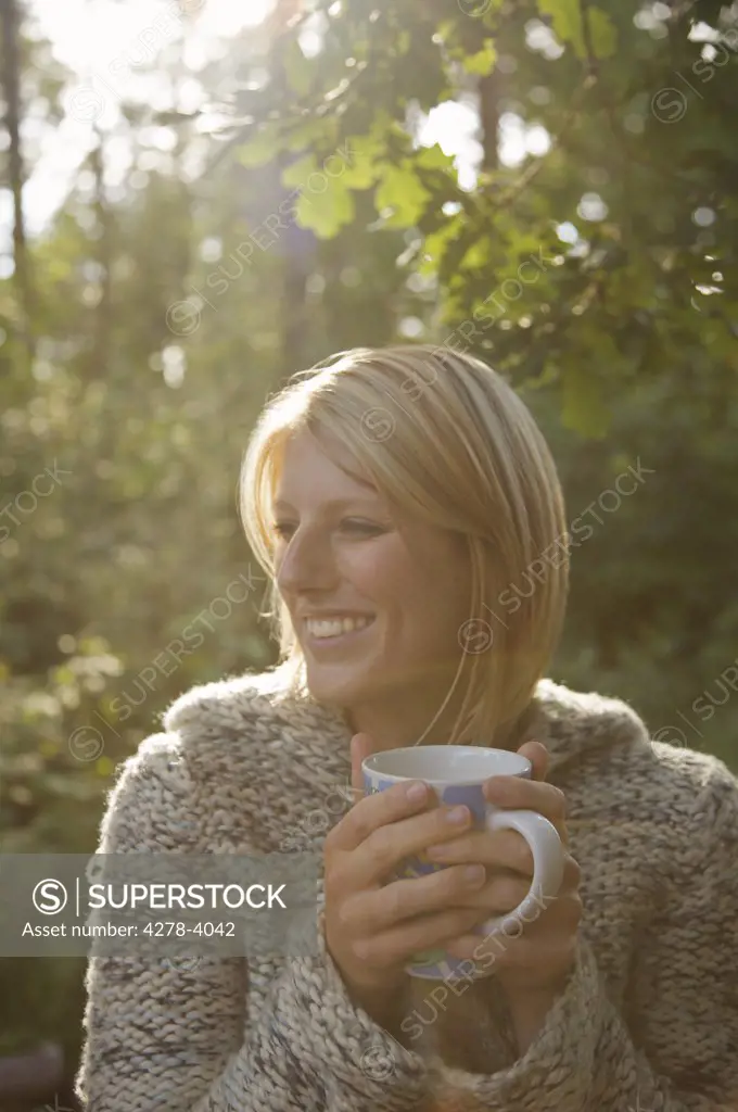 Smiling young woman in a forest holding a mug looking to one side