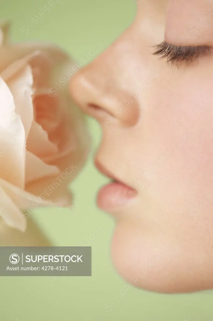 Extreme close up of a young woman profile inhaling a pink rose