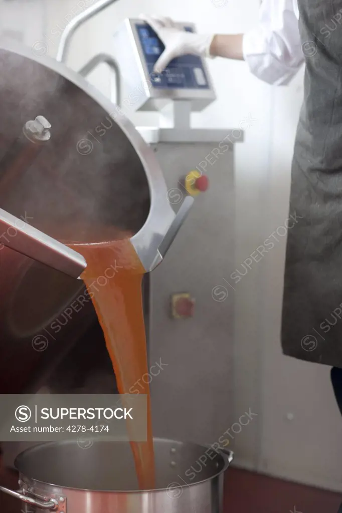 Factory worker using computer controlled machinery pouring tomato sauce into a pan