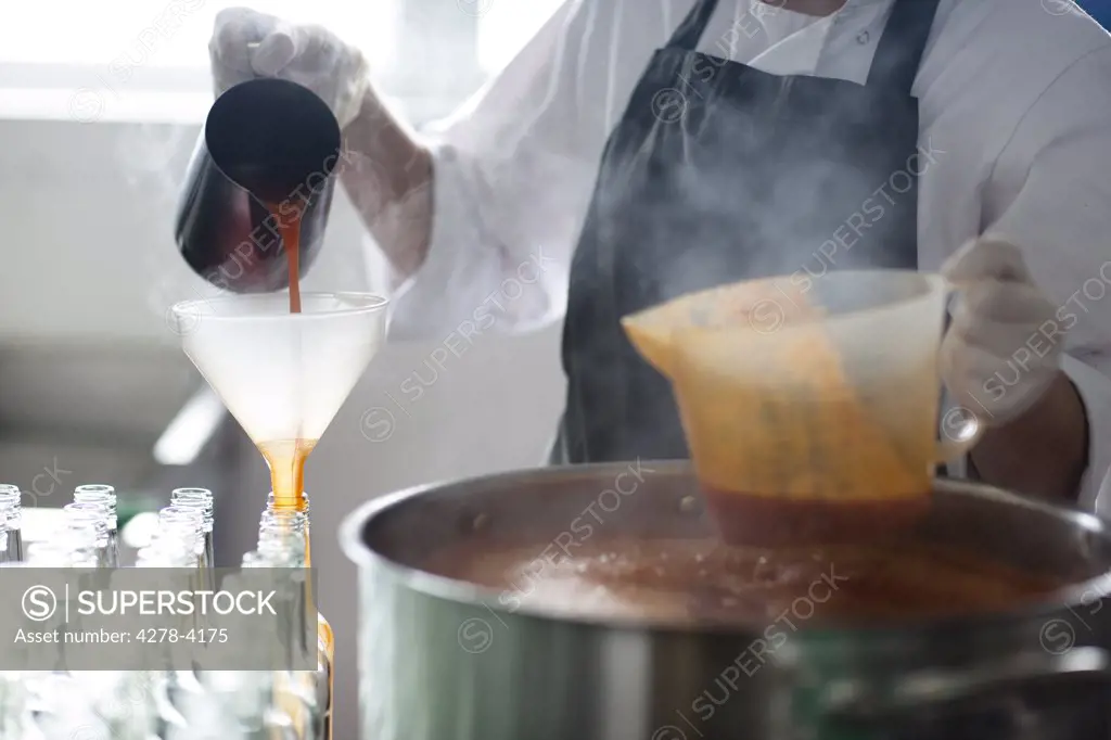 Factory worker pouring tomato sauce through a funnel into bottles