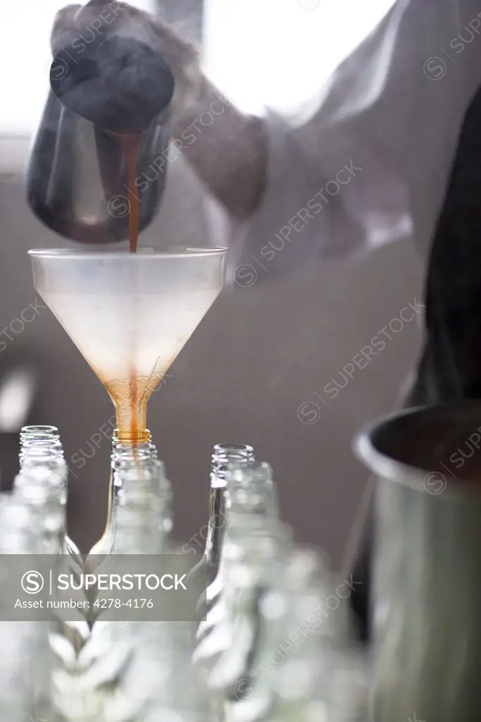 Factory worker pouring tomato sauce through a funnel into bottles