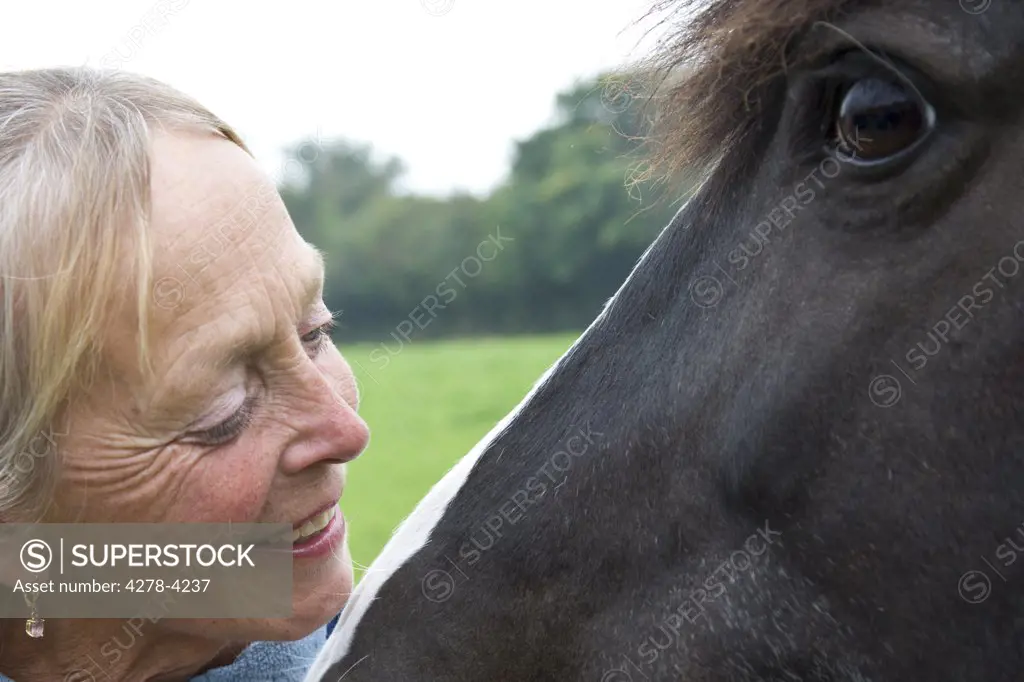 Close up of a smiling mature woman next to horse head
