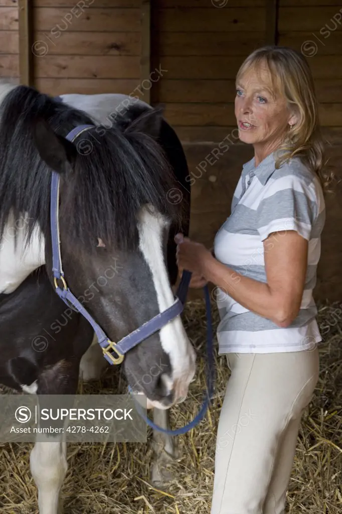 Mature woman standing next to a horse holding bridle