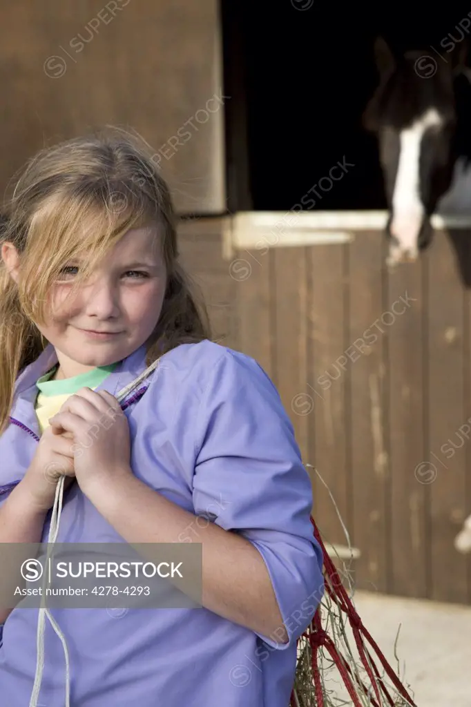 Young girl standing in front of stable carrying a net bag over her shoulder