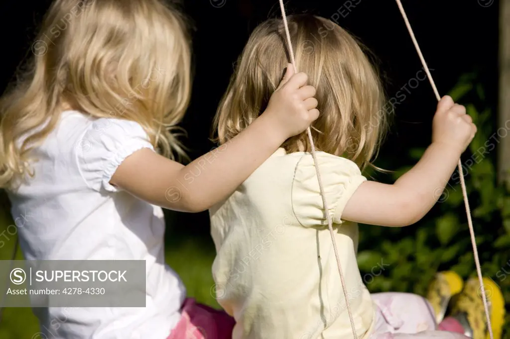 Back view of two young girls on swing