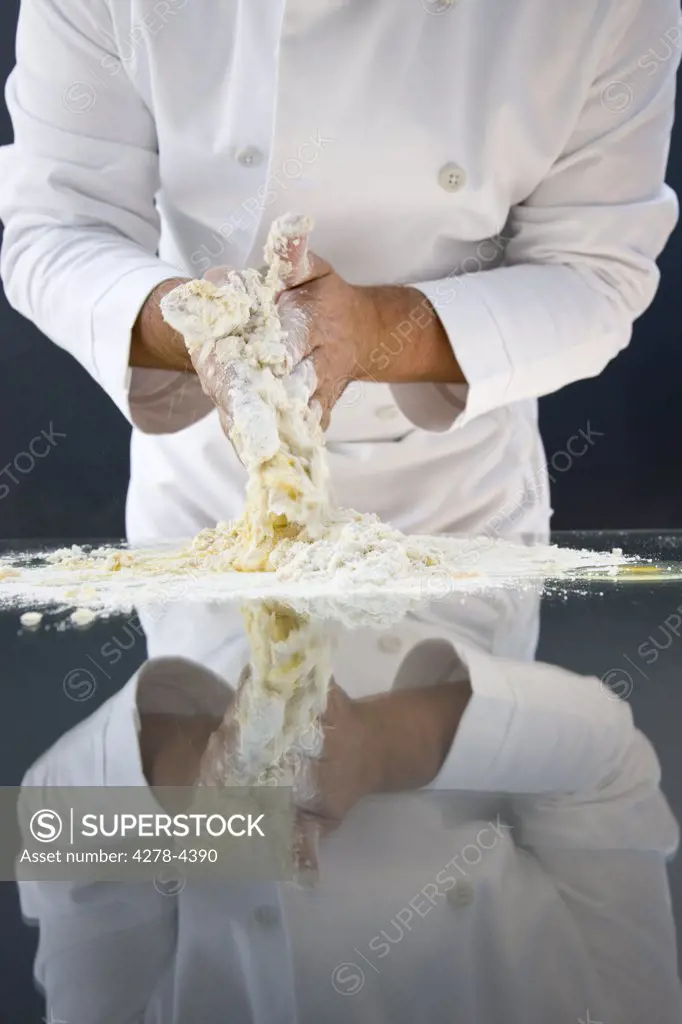 Close up of a chef hands making a dough with egg and flour over a glass table