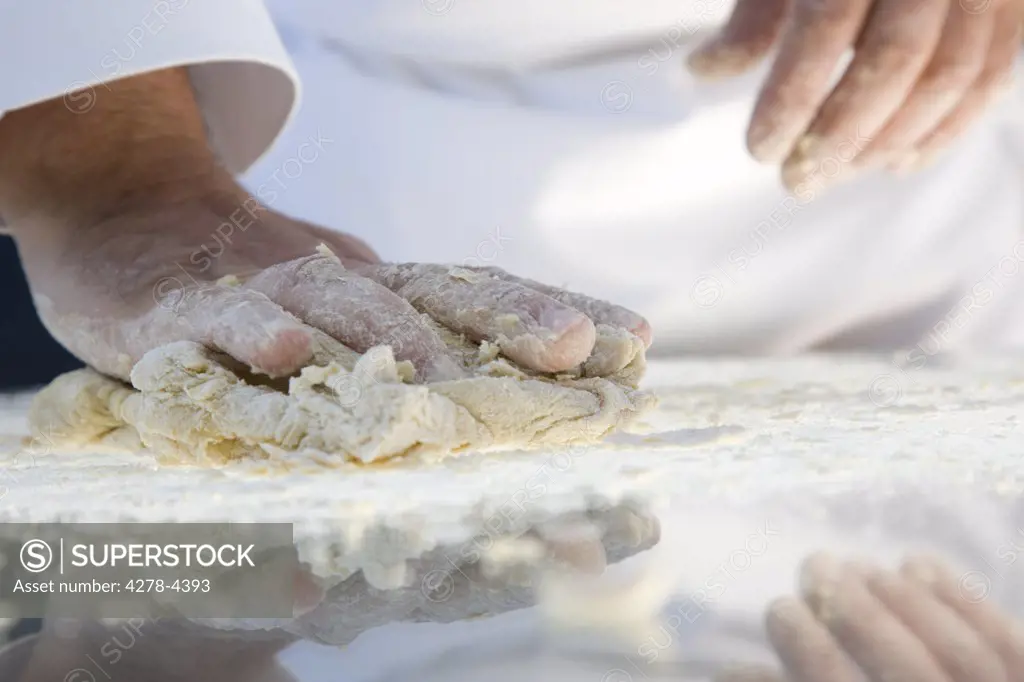 Close up of a chef hands kneading pasta dough over a glass table