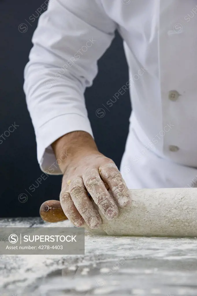 Close up of a chef hand rolling dough with a wooden rolling pin