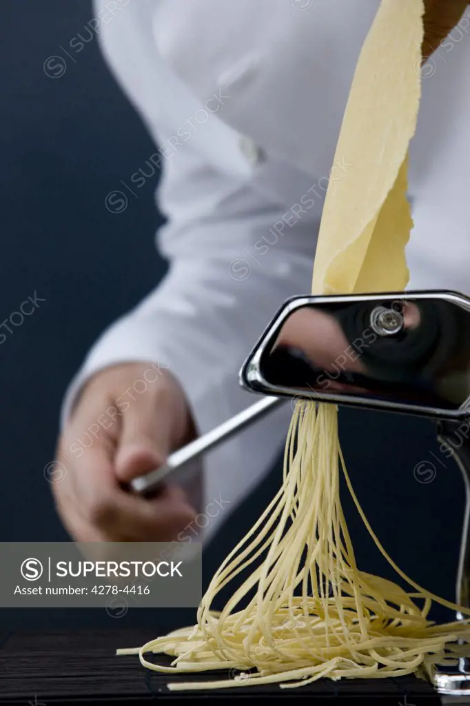 Close up of a chef hand turning the handle of a pasta maker with tagliolini coming out
