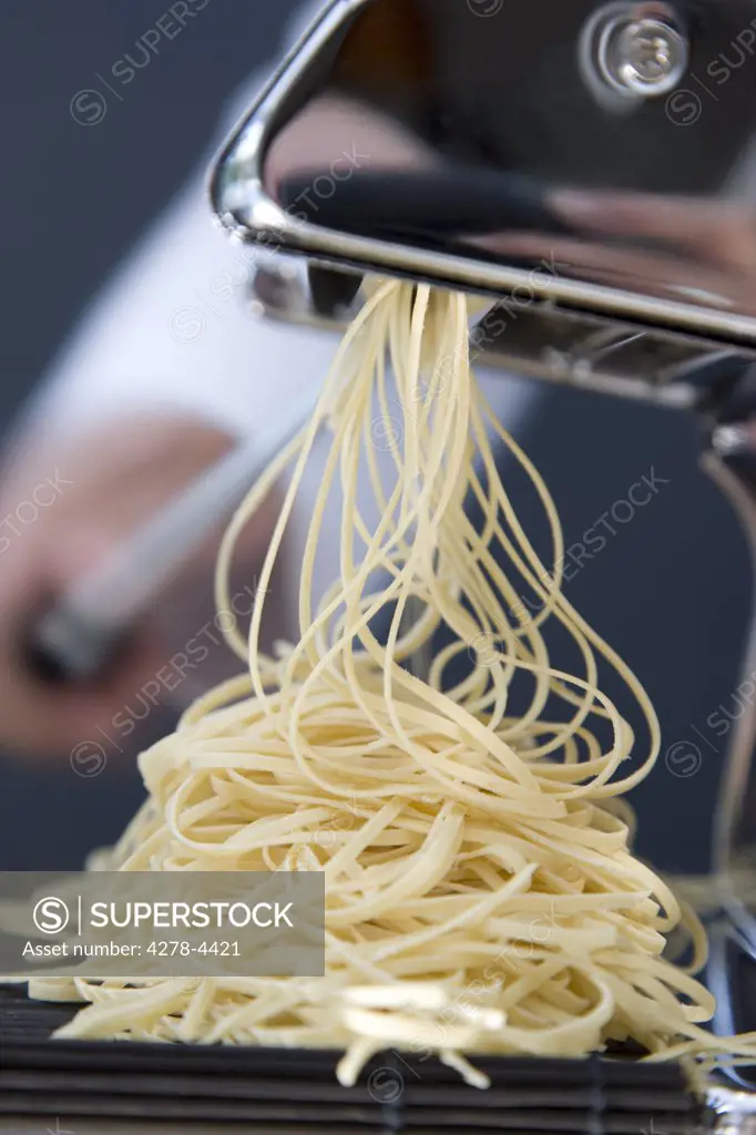 Heap of fresh tagliolini coming out of a pasta maker with hand turning the handle