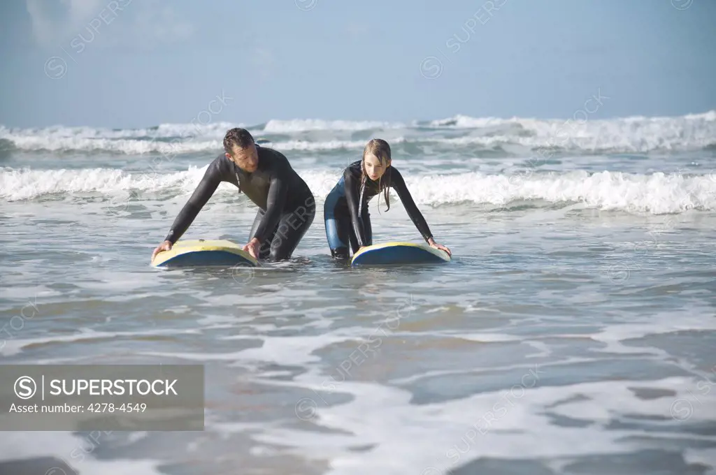 Man and girl crouching in the sea holding on to their surfboards