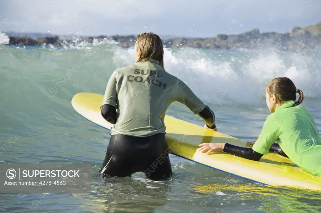 Back view of a woman in the sea holding a surfboard with a girl lying on it
