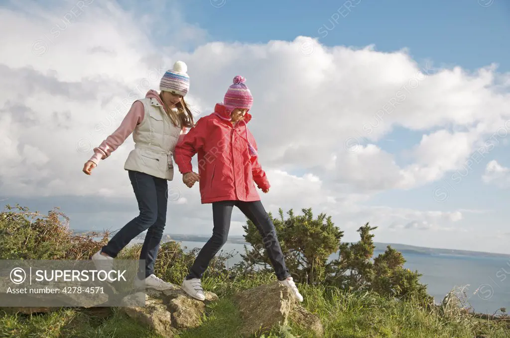 Two young girls walking on top of a cliff