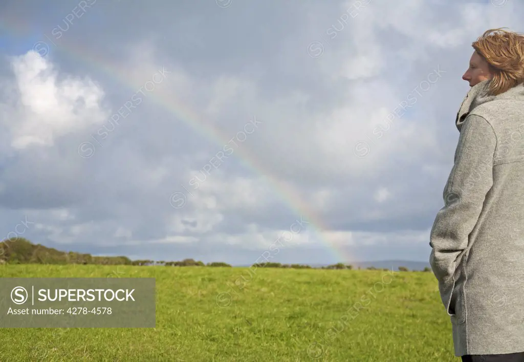 Woman standing in a field looking at the rainbow