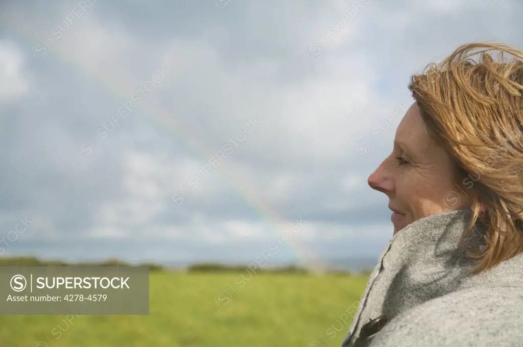 Close up of a woman standing in a field looking at the rainbow