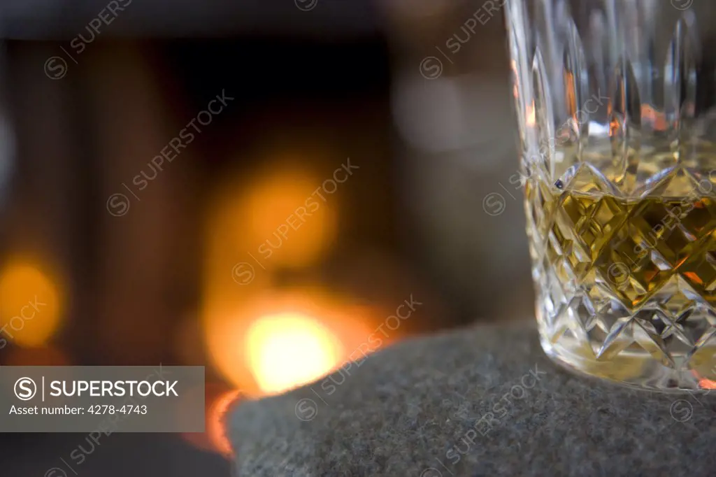 Close up of a glass of whiskey in front of a fireplace