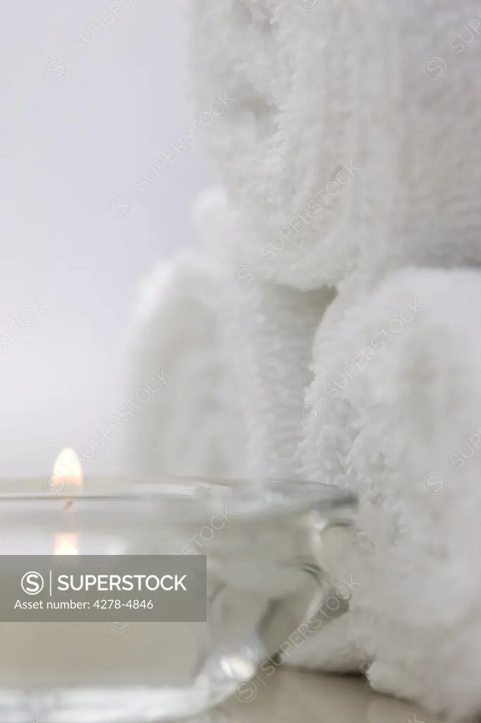 Close up of a burning tea light and rolled up white towels