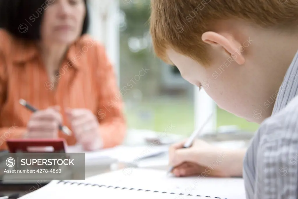 Close up of a boy doing homework with  woman supervising