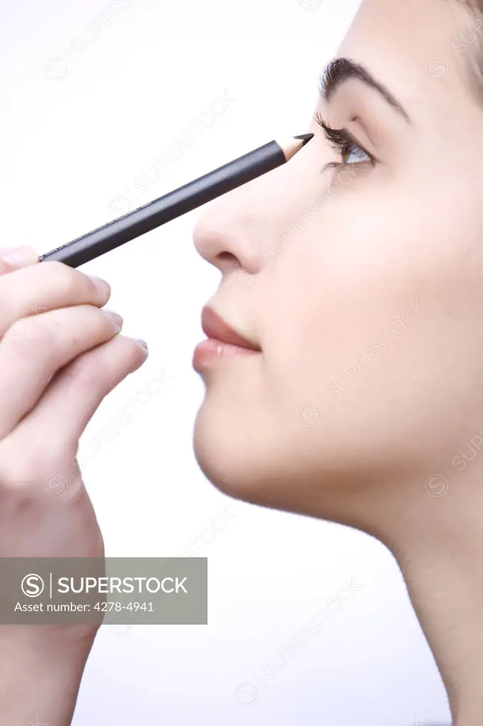 Profile of a young woman applying make on her eye with a pencil - close up