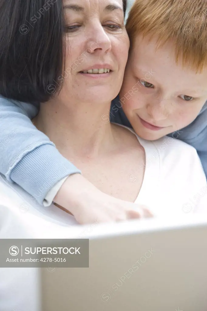Boy hugging woman whilst looking at laptop computer monitor