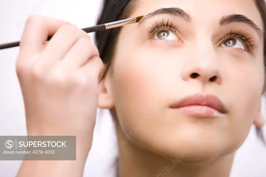 Close up of a young woman applying make up on her eyebrow with a brush