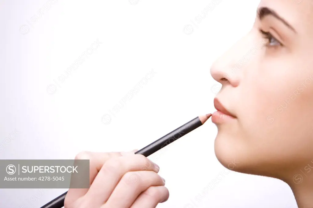 Profile of a young woman applying make on her lips with a lip pencil - close up
