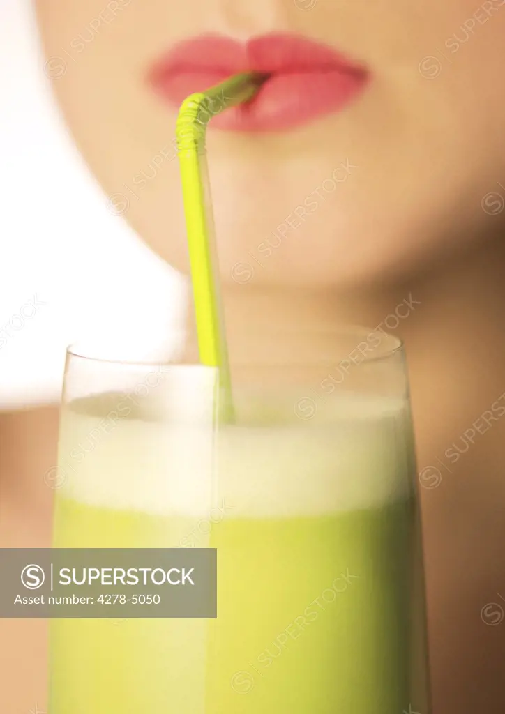 Close up of a woman mouth drinking a vegetable smoothie with a straw
