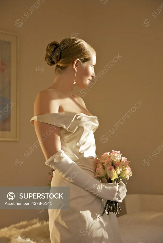 Profile of a bride in a white wedding gown holding a bouquet of roses
