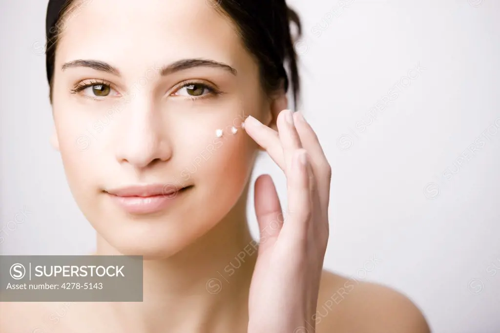 Close up of a young woman applying moisturizer on her cheek