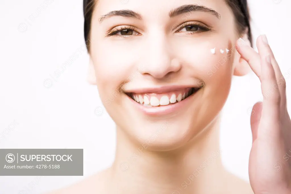 Close up of a smiling young woman applying moisturizer on her cheek