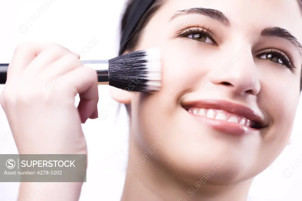 Close up of a smiling woman applying make with a blush brush